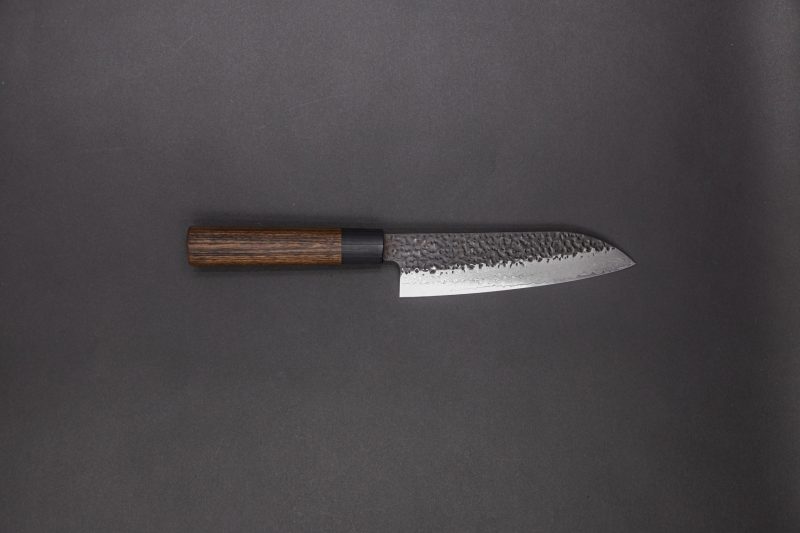 Gen - Gyuto 210mm kaufen: Dieses japanische Küchenmesser hat einen dunklen Holzgriff und eine gehämmerte Stahlklinge, präsentiert vor schlichtem dunkelgrauem Hintergrund.