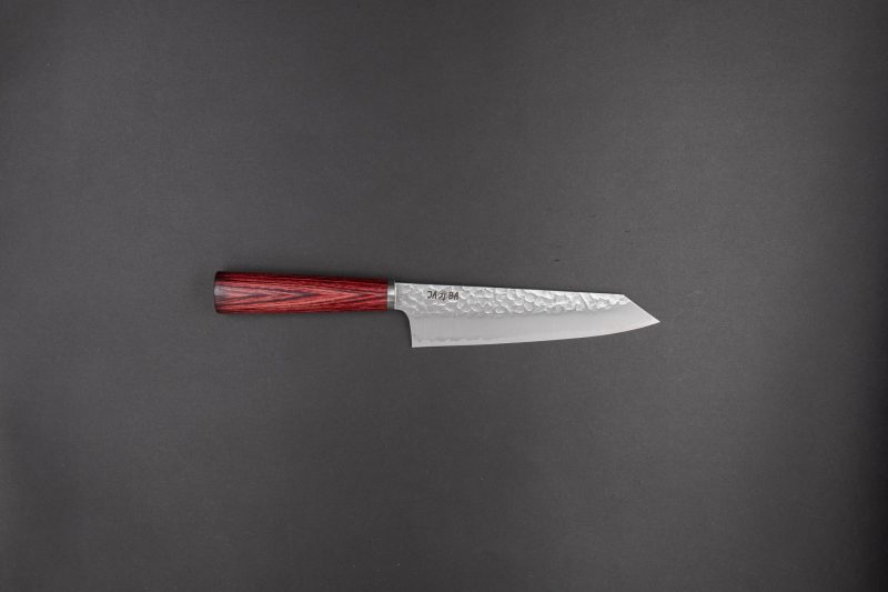 Ein Küchenmesser im japanischen Stil mit gehämmerter Silberklinge und dunkelrotem Holzgriff, dargestellt auf einem schlichten dunkelgrauen Hintergrund.
