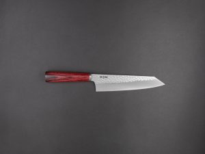 Ein Küchenmesser im japanischen Stil mit einer Klinge aus gehämmertem Stahl und einem dunkelroten Holzgriff, waagerecht auf einem schlichten dunkelgrauen Hintergrund angeordnet.