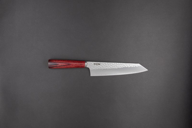 Ein Küchenmesser im japanischen Stil mit einer Klinge aus gehämmertem Stahl und einem dunkelroten Holzgriff, waagerecht auf einem schlichten dunkelgrauen Hintergrund angeordnet.