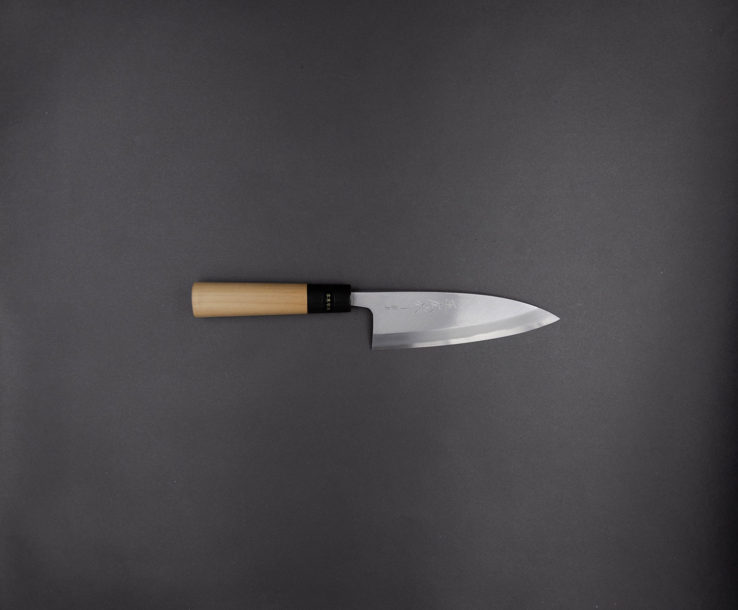 Ein japanisches Küchenmesser mit Holzgriff und glänzender, scharfer Klinge ist waagerecht auf einem schlichten dunkelgrauen Hintergrund platziert.