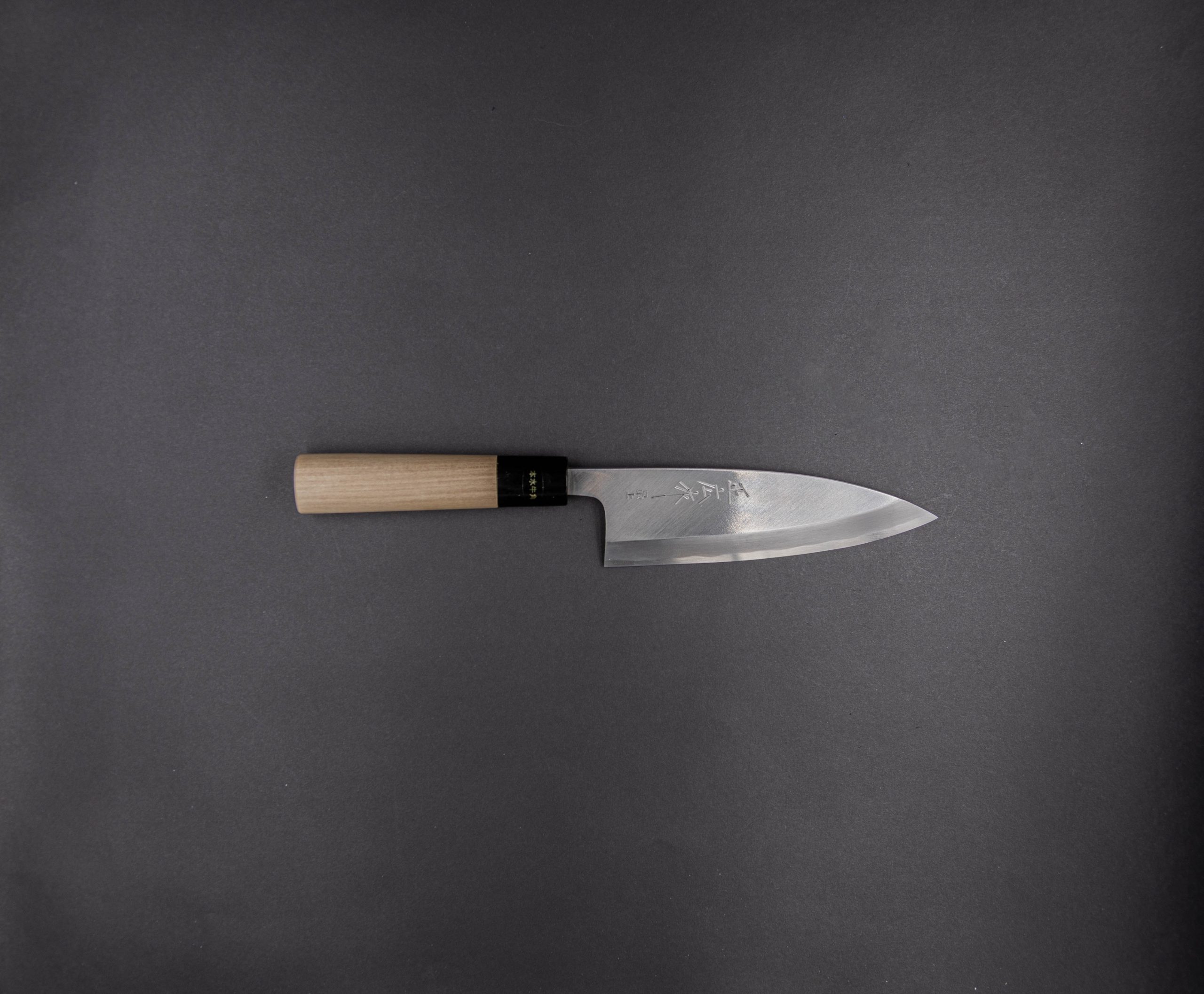 Ein einzelnes japanisches Kochmesser mit Holzgriff und glänzender, leicht gebogener Klinge ist waagerecht auf einem dunkelgrauen Hintergrund platziert.