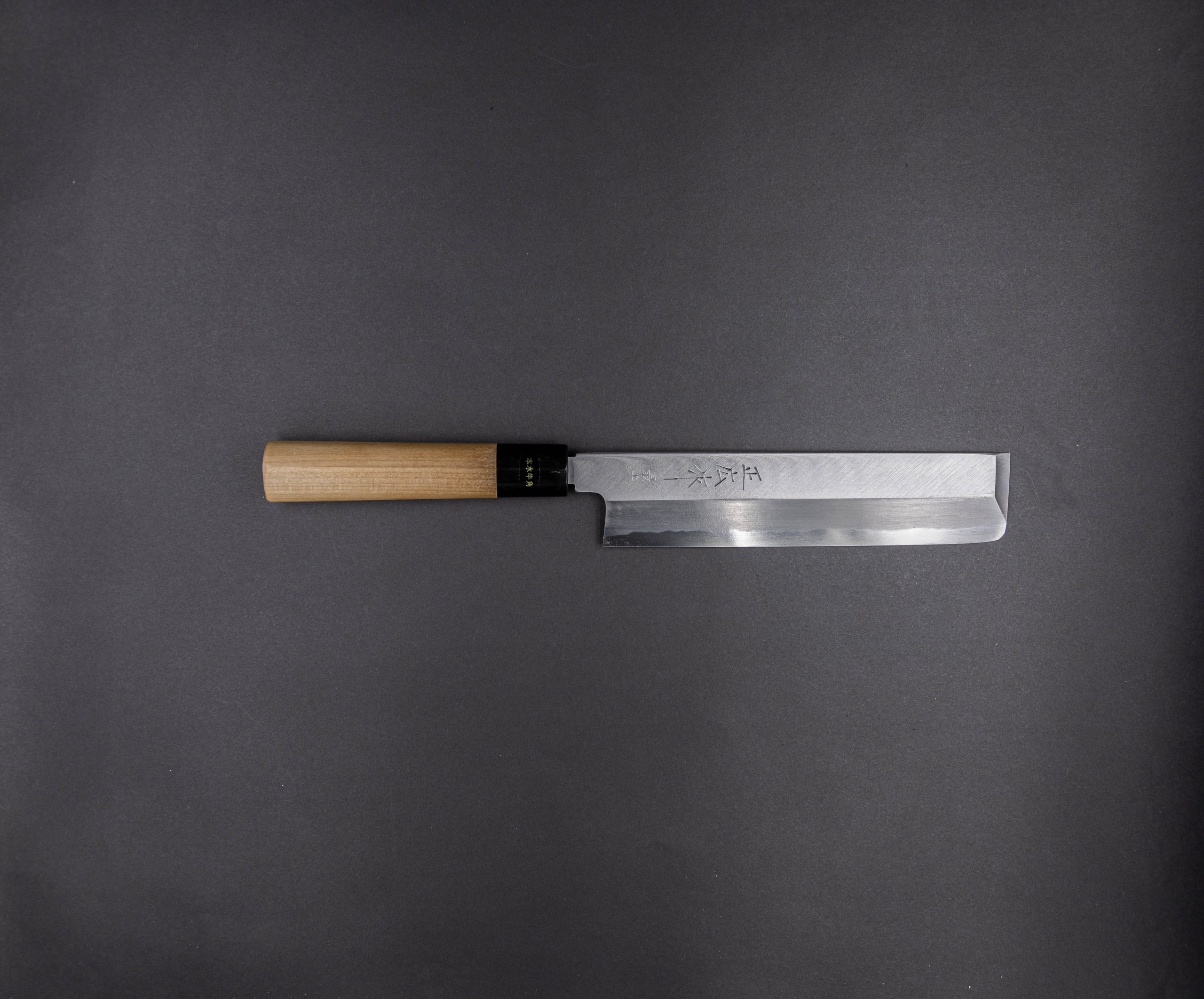 Ein Küchenmesser im japanischen Stil mit gerader Klinge und Holzgriff ist horizontal auf einem dunkelgrauen Hintergrund platziert.